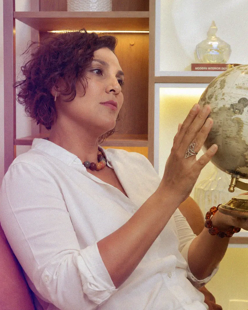 Ju Bella, professora de inglês, sentada segurando um globo terrestre antigo em seu escritório.