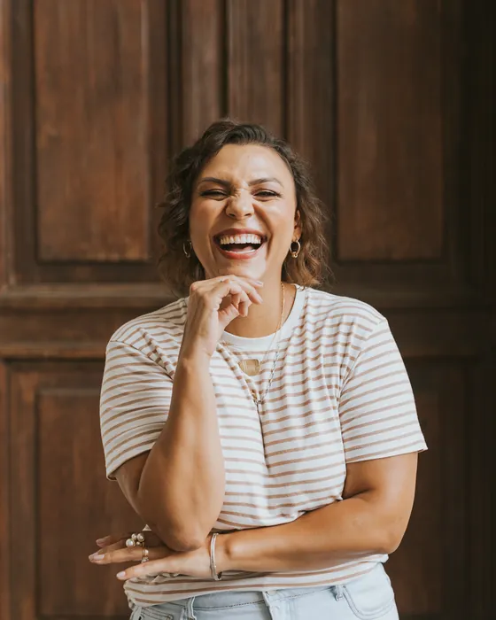 Professora Ju Bella rindo, com a mão no queixo
