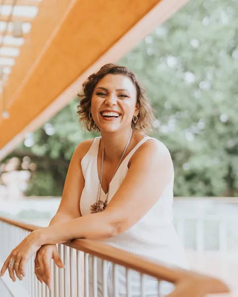 Ju Bella rindo, apoiada no parapeito de uma varanda
