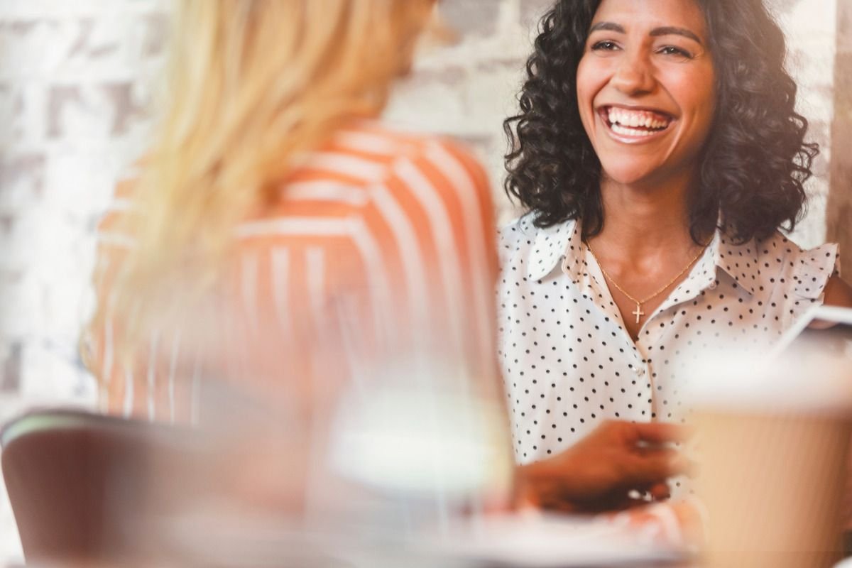 Duas mulheres conversando e rindo em uma mesa de café