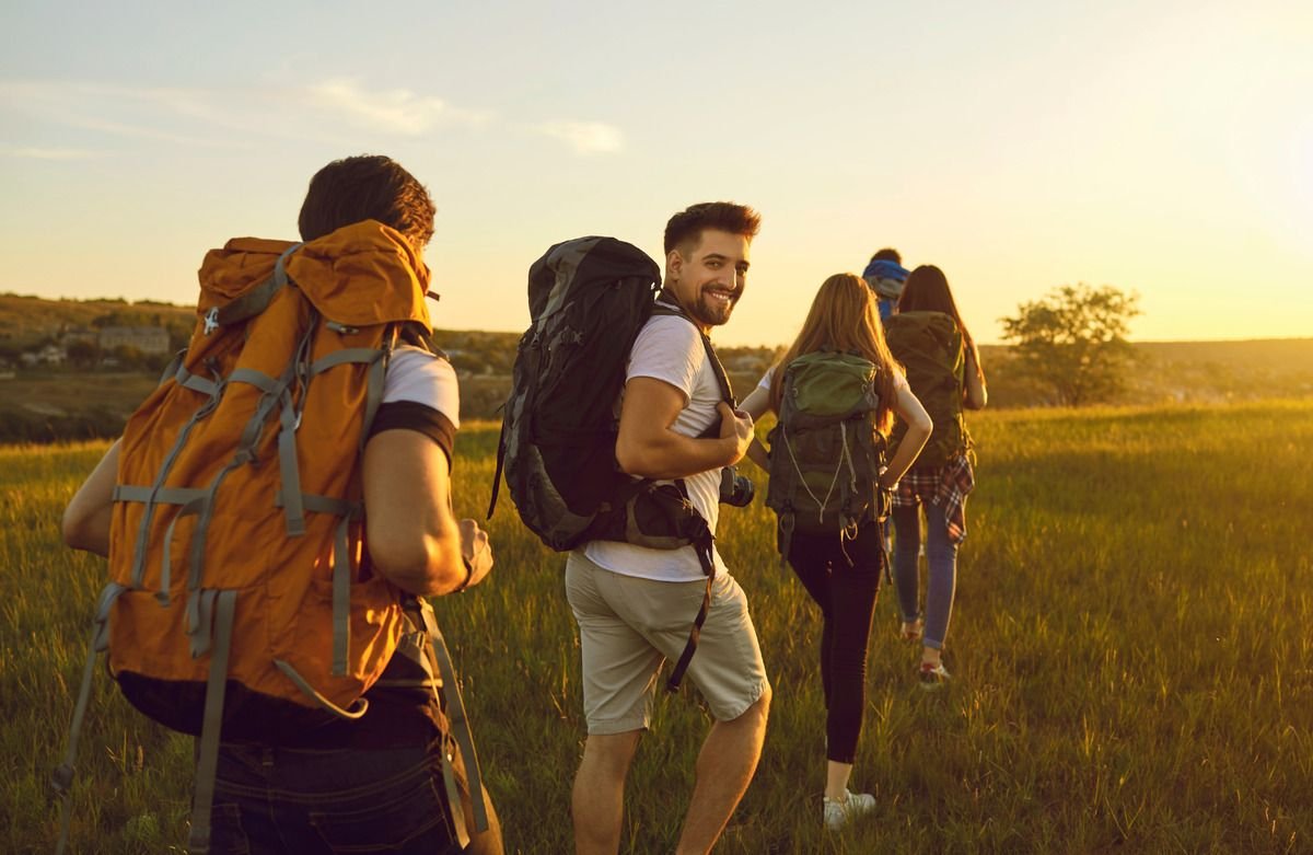 Grupo de amigos com mochilas caminhando ao pôr do sol durante uma viagem